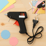 A black and red glue gun with a European plug and cord, with two scalloped paper cutouts and craft paper.