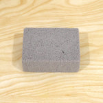 A single gray rectangular cleaning block with a porous texture centered on a light wooden surface.