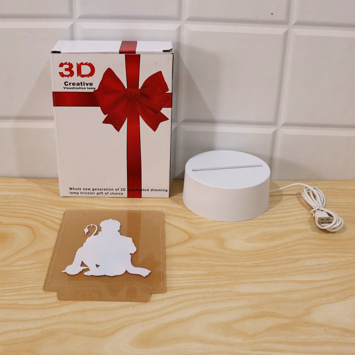 The Hanuman LED lamp components laid out: a gift box, the white base with cable, and the acrylic panel.