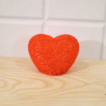 A textured orange heart-shaped LED lamp is centered on a light wooden surface against a white tiled wall.