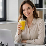 A smiling woman in a beige shirt holds a yellow silicone cup with a dome lid and straw while sitting at a desk with a laptop.