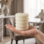 A single cream ribbed LED candle is held in an open palm, with a blurred living room background.