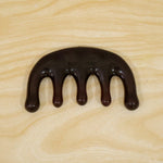 A dark brown resin scalp massager with five rounded prongs is centered on a light wooden surface.