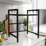 Empty black metal microwave oven rack on a white countertop with a plant and oil bottles in the background.