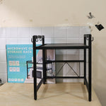 Black metal microwave oven storage rack on a light wooden surface, with its product box visible behind it.