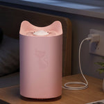 A pink cat-shaped mosquito lamp with an embossed cat design is plugged into a wall socket on a wooden nightstand.