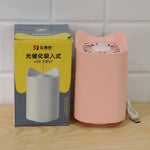 A pink cat-shaped mosquito lamp and its yellow and white product box are displayed on a wooden surface.