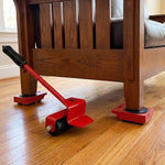 A red furniture lifter tool is shown under a wooden chair leg, with three red wheeled sliders already in place.