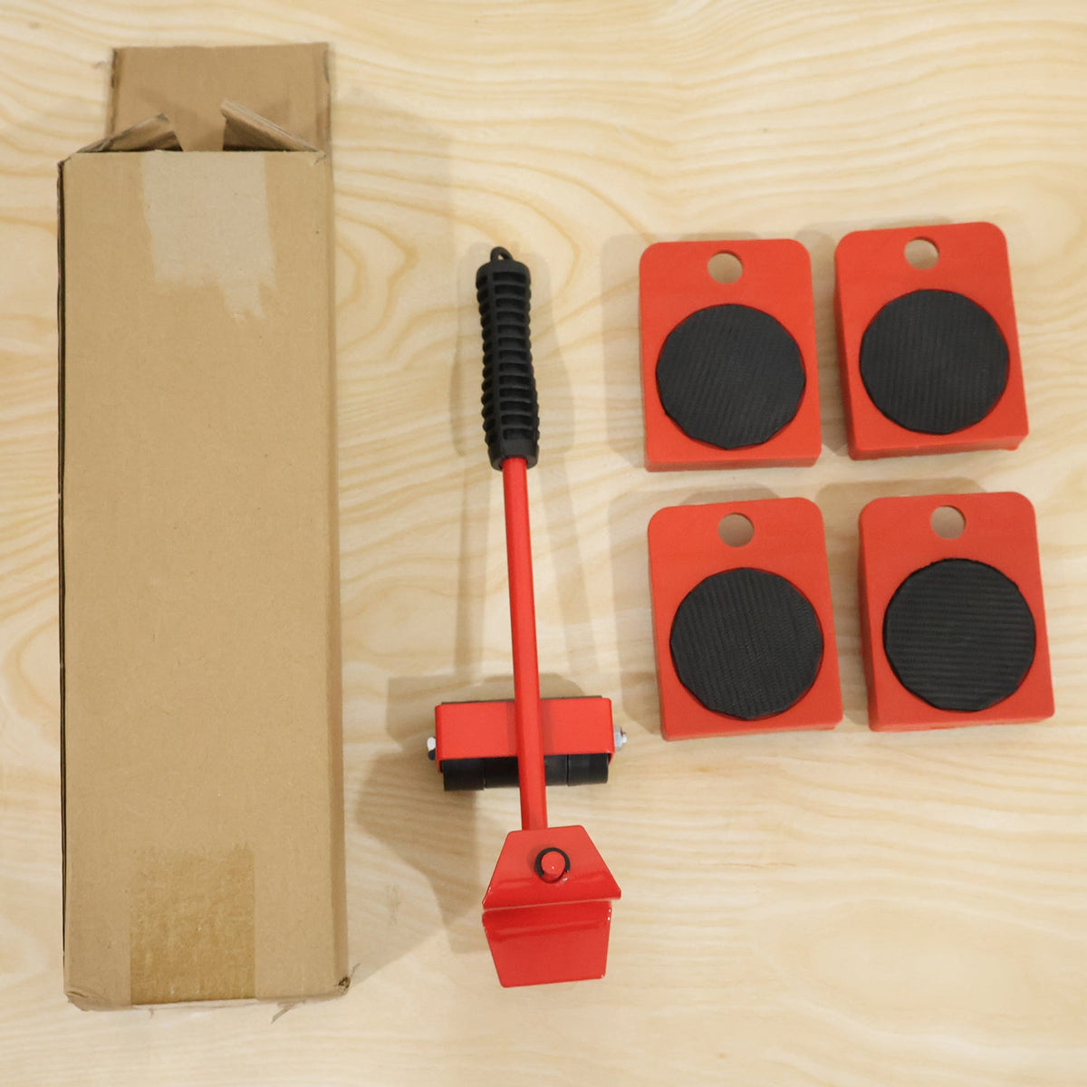 The red furniture lifter and four wheeled sliders are displayed next to an open cardboard box on a light wooden surface.