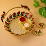 A golden kumkum dish with a peacock handle, holding red kumkum and white rice, with two lidded containers on a light brown