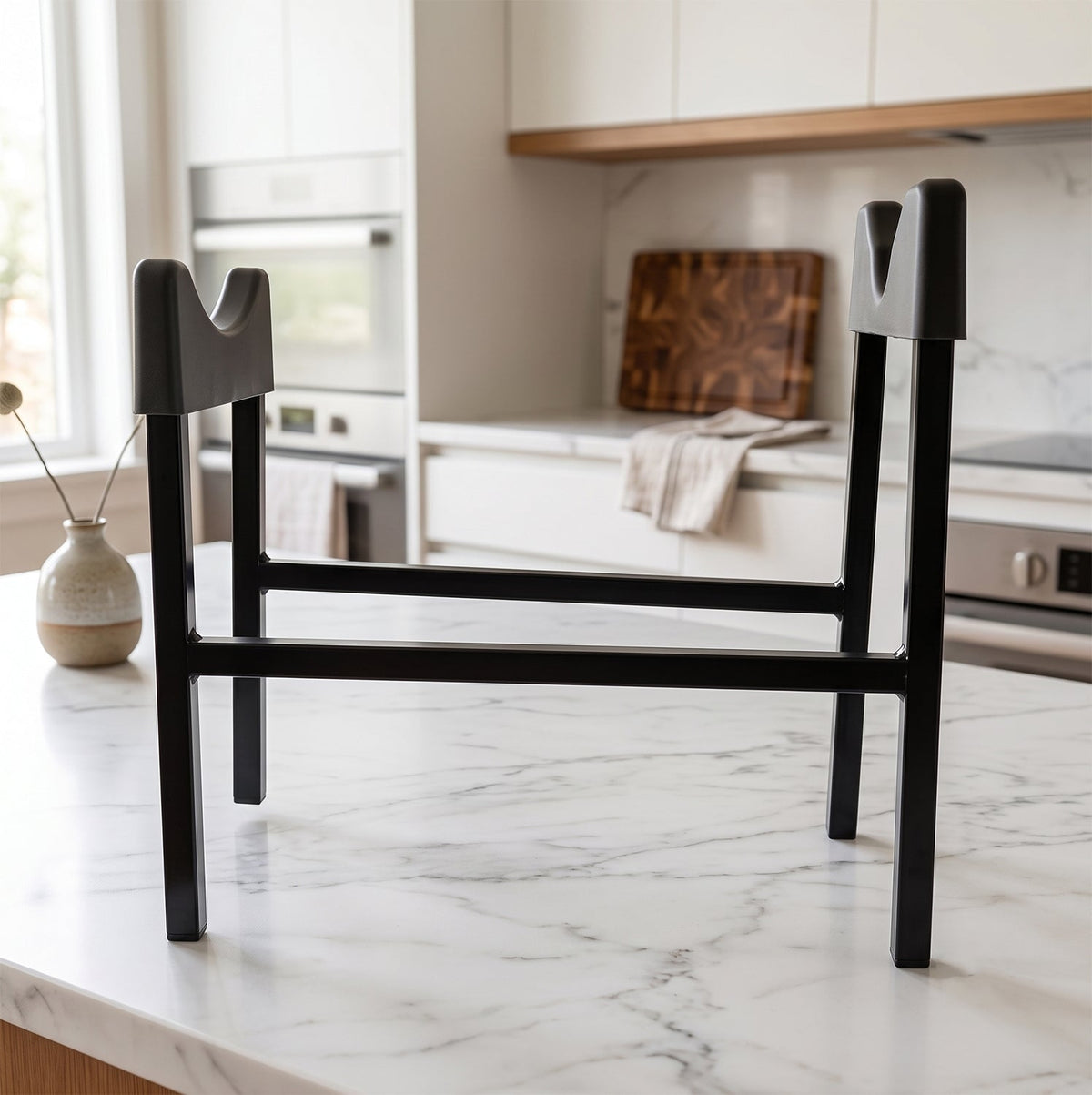 A black metal water bottle stand sits on a white marble kitchen counter with modern appliances in the background.