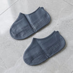 A pair of gray silicone foot coverings with textured soles rests on a light gray tiled surface.