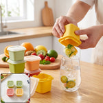 A person dispenses a citrus-infused ice cube from a yellow mold into a glass of water on a wooden counter, surrounded by