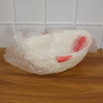 A white whale-shaped rice drainer bowl with red accents is wrapped in clear plastic packaging on a wooden surface.
