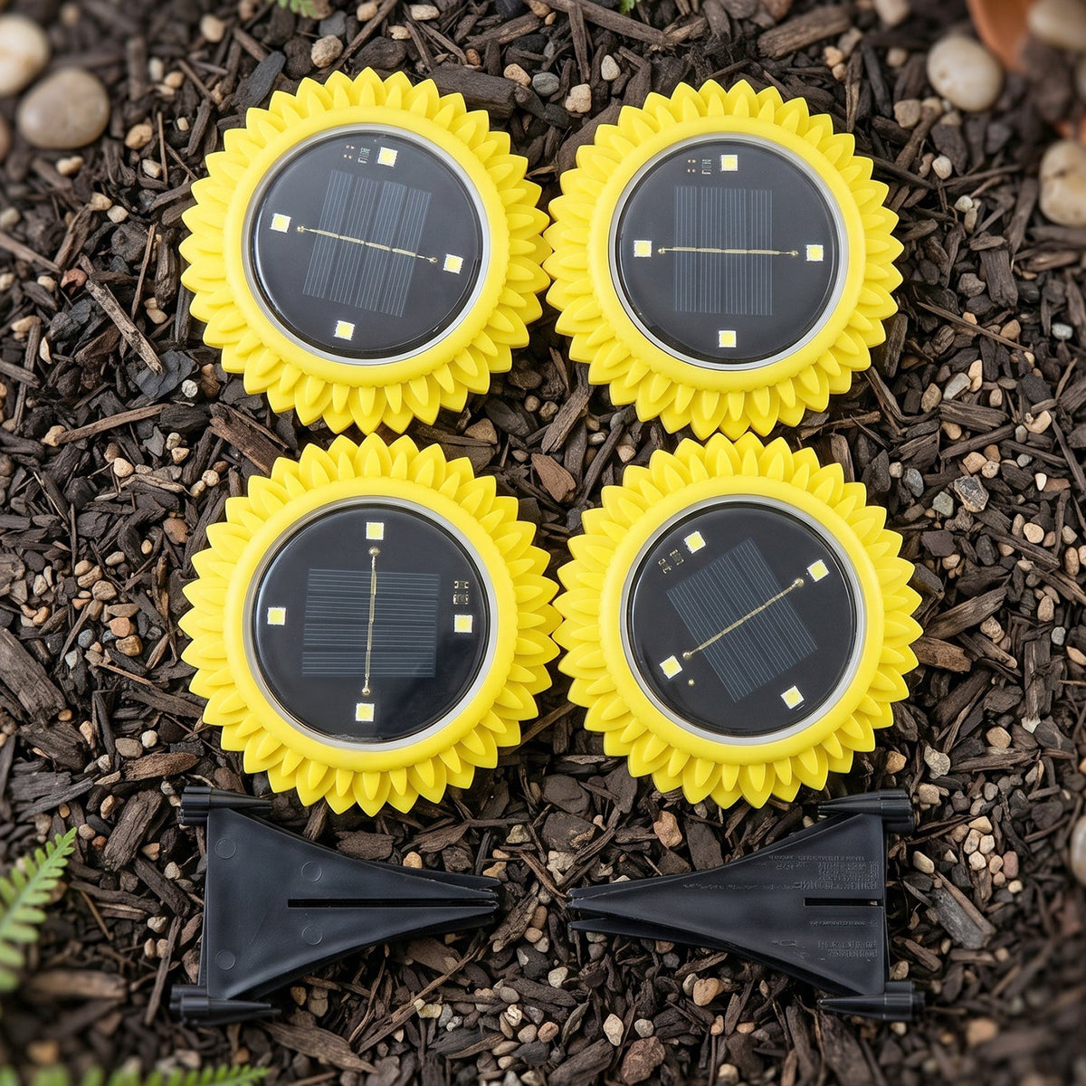 Four yellow, sunflower-shaped solar lights with black solar panels and two black ground stakes are arranged on dark soil.