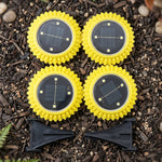 Four yellow, sunflower-shaped solar lights with black solar panels and two black ground stakes are arranged on dark soil.