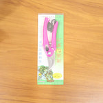 The pink garden pruner is sealed in its clear plastic and green cardboard retail packaging on a wooden surface.