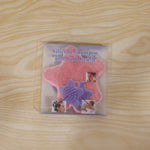 A pink silicone starfish-shaped brush is visible inside clear plastic packaging, featuring images of people using it on a