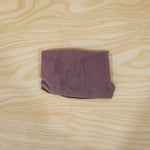 A deflated purple velvet U-shape neck pillow is folded neatly into a compact rectangle on a light wooden surface.