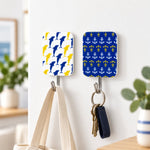 Two decorative adhesive hooks on a white wall, one holding a beige tote bag, the other a set of keys.