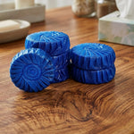 Several blue, round toilet cleaner tablets with a spiral pattern are stacked on a wooden surface.