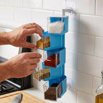 A person's hands are shown filling the clear containers of a blue 5-layer rotating spice rack with various spices.