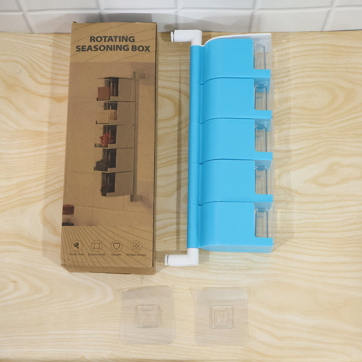 A blue 5-layer rotating spice rack, its cardboard box, and two adhesive hooks are displayed on a wooden surface.