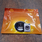 An orange powder sachet with a washing machine drum and miniature washing machine graphic on a dark wooden surface.
