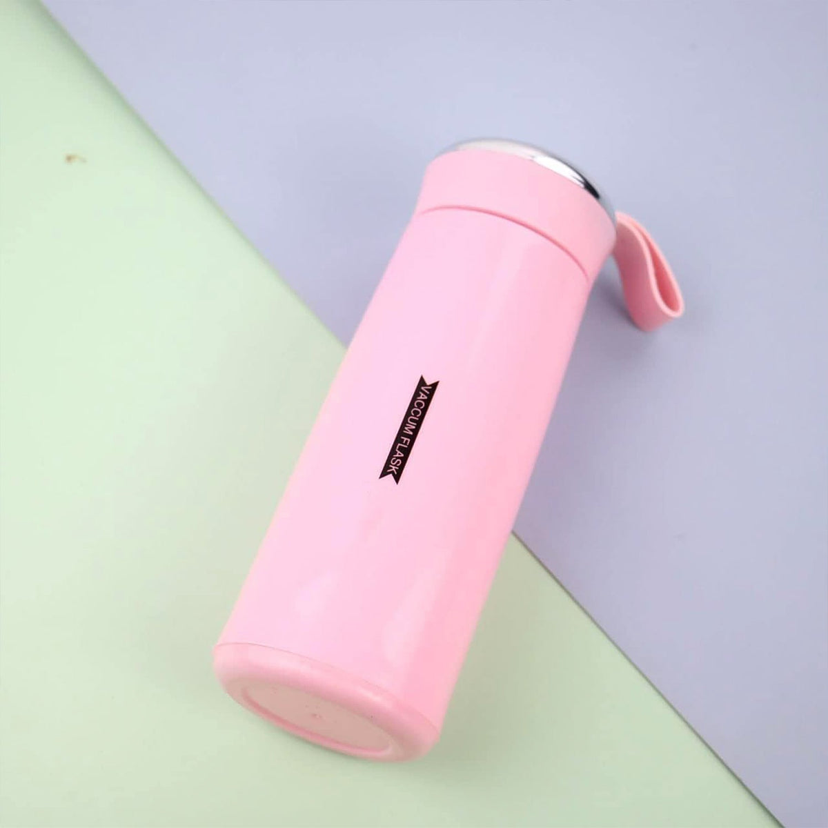 A pink vacuum flask with a silver lid and strap lies diagonally on a light blue and green background.