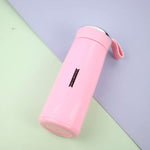 A pink vacuum flask with a silver lid and strap lies diagonally on a light blue and green background.