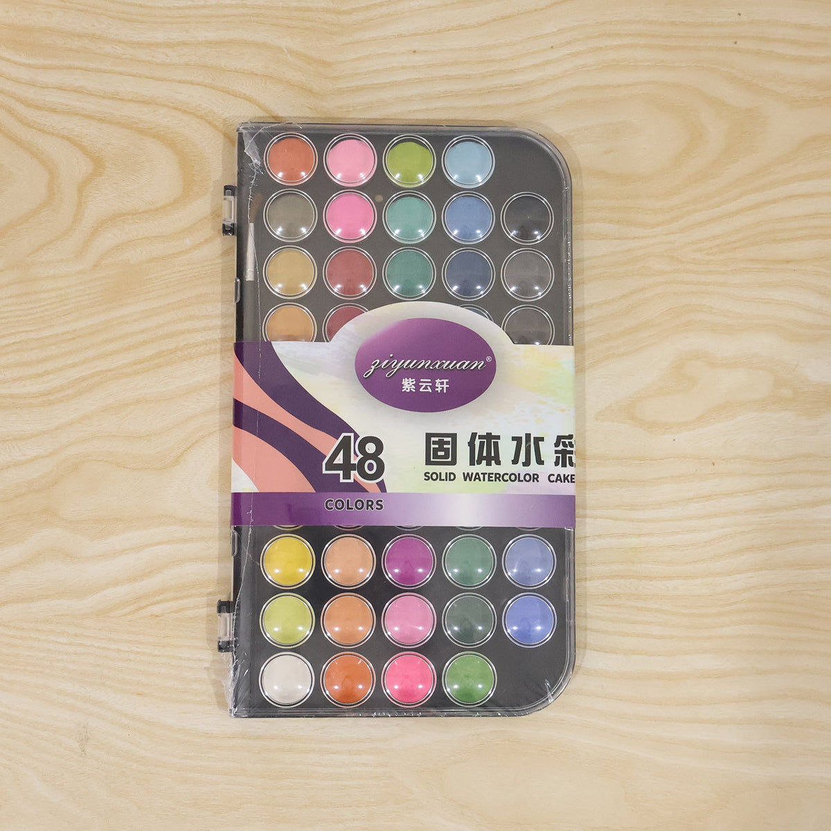 A packaged 48-color solid watercolor cake set with Chinese text on a wooden surface.