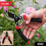 A hand holds red and black pruning shears to cut a pink dahlia stem, with an inset showing the shears on wood.