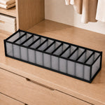 An empty gray 11-section fabric organizer with black trim sits on a light wooden dresser in a closet.