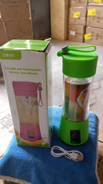 A green portable juicer blender with a white USB cable is next to its box on a blue towel, surrounded by cardboard boxes.