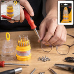 A person uses a red and black screwdriver to tighten a screw on a pair of glasses, with the screwdriver set and other tools.