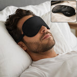 A man with a beard sleeps peacefully on a white pillow, wearing a black sleeping eye mask with an adjustable strap.