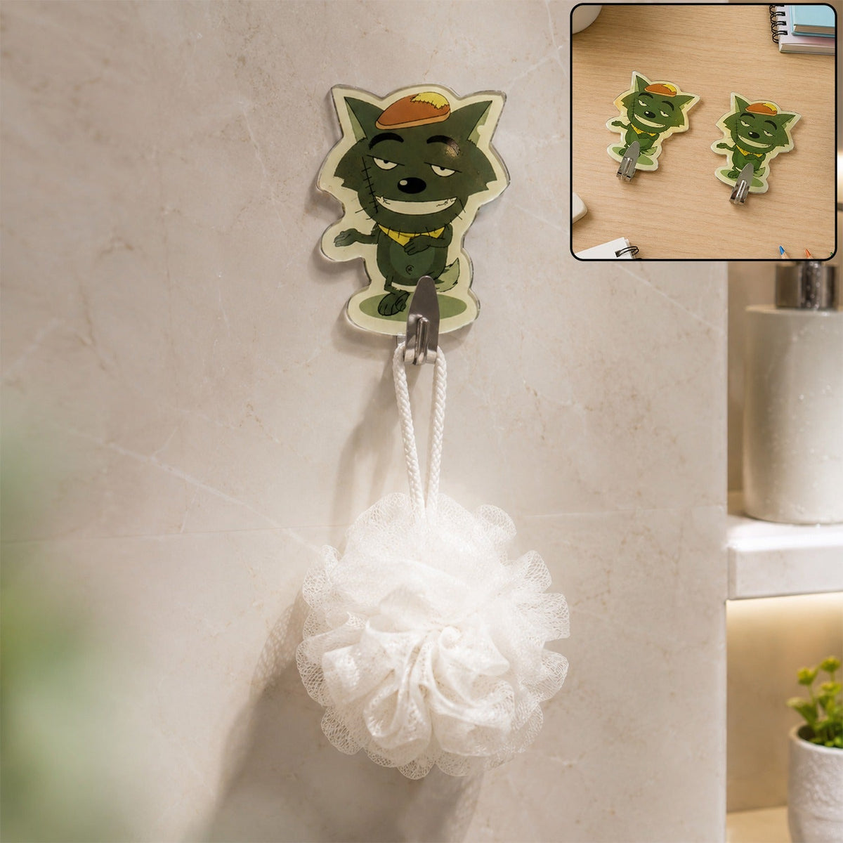 A green cartoon wolf hook holds a white bath pouf on a tiled bathroom wall, with an inset of two wolf hooks on a desk.