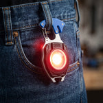 A black and silver multifunction keychain light with a blue clip hangs from a jean belt loop, emitting a bright red – view 7