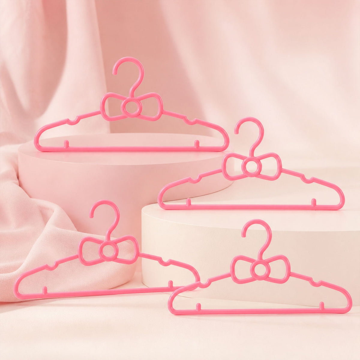 Four pink plastic bow-shaped hangers are arranged on and around two pink display blocks on a pink background.