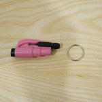 A pink emergency tool with a black clip and a separate silver keychain ring are placed on a light wood grain surface.