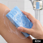A hand holds a blue exfoliating sponge with animal patterns, scrubbing a leg with soap suds.