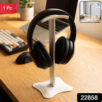 White headphone stand with black headphones on a wooden desk, a laptop, and a small plant in the background.