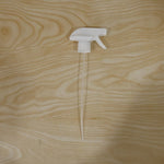 A white plastic spray nozzle with a long, clear tube is centered on a light wooden surface with visible grain.